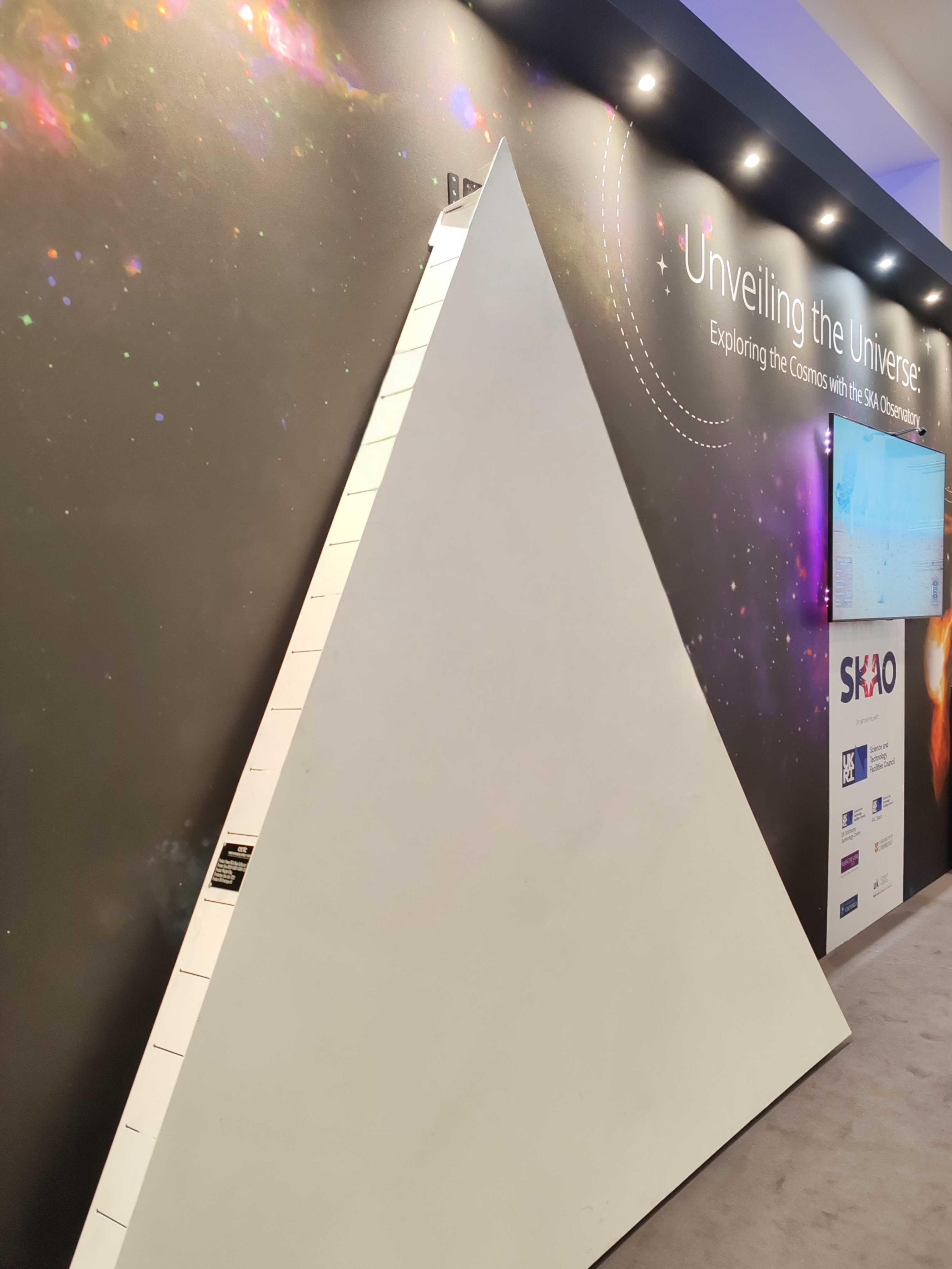 A metal triangular panel, standing at the front of the SKAO's exhibit.
